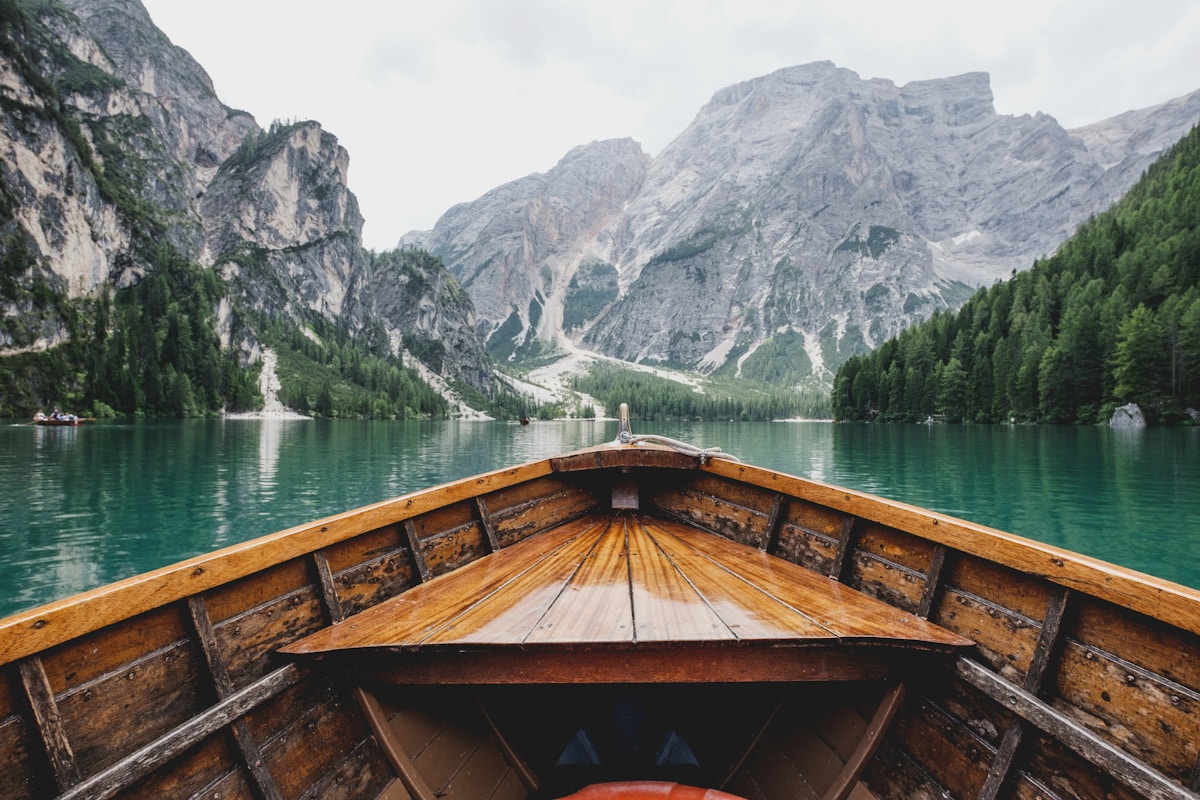 The bow of a wooden boat on a green alpine lake below rock faces