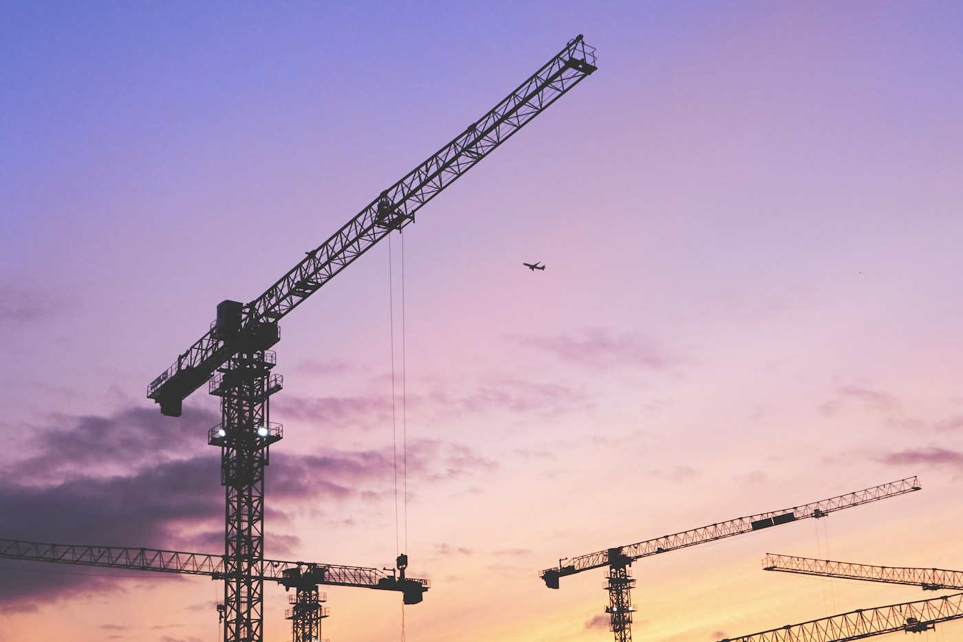 Tower cranes silhouetted against a purple evening sky